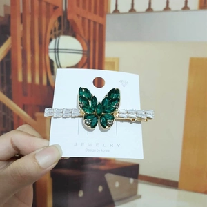 Close-up of golden butterfly hair clip featuring green and clear zircon crystals