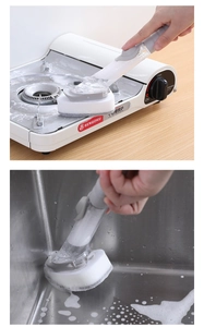 Detail showing the gray handle kitchen brush cleaning a gas stove and stainless steel sink
