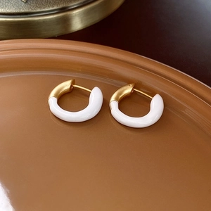 Detailed close-up of gold and white enamel heart earrings on a warm brown tray