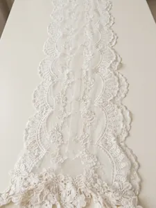 Detailed view of the intricate floral embroidery and wavy lace edge on white scarf fabric