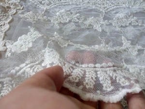 Close-up of white floral embroidery and scalloped edge detail on lace scarf fabric