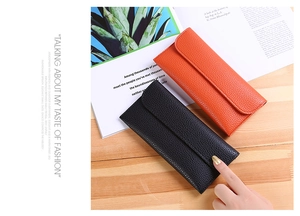 Detail of slim lychee texture leather wallets in black and orange on a fashion magazine
