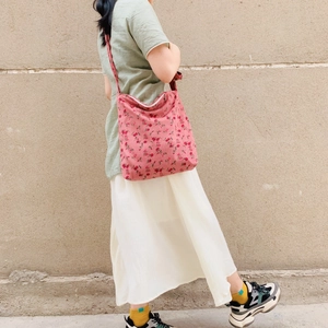 Pink corduroy crossbody bag with red floral pattern worn by a model against a stone wall