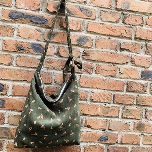 Green corduroy shoulder bag with gold leaf pattern against a brick wall background