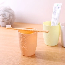 Detail of travel toothbrush cups in orange and yellow on a wooden bathroom counter