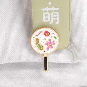 Close-up of a magnifying glass enamel pin with microbial patterns on a canvas strap