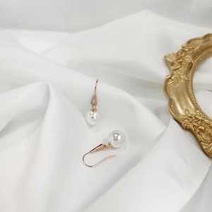 Dettaglio degli orecchini di perle in argento 925 su raso bianco con cornice dorata