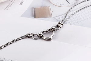 Detail of a stainless steel box chain necklace with a hollow heart pendant on a stone surface