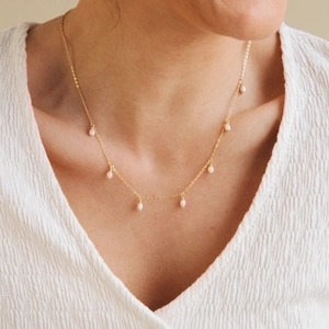 Close-up of minimalist gold chain necklace with cascading oval pearls on a model neck