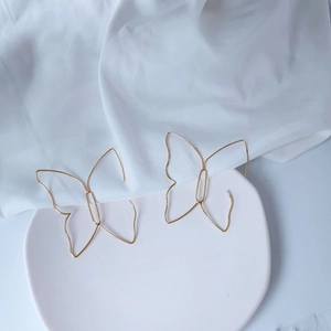 Dettaglio di orecchini a farfalla traforati in oro 14K su un piatto di ceramica opaco