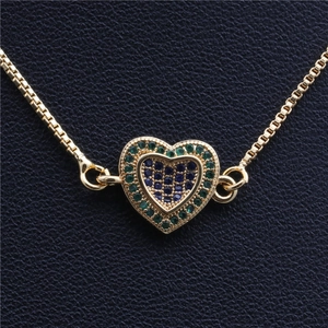 Vue macro du pendentif cœur doré avec zircons bleus et verts sur chaîne vénitienne
