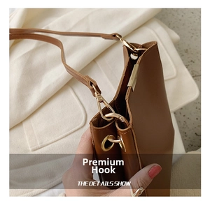 Detail of brown leather bucket bag featuring a polished gold metal swivel hook and fine stitching