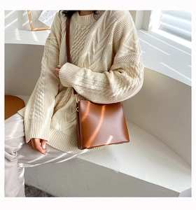 Brown leather bucket bag styled with a white knit sweater in soft natural window light