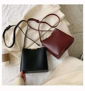 Detail of elegant black and burgundy leather bucket bags with gold hardware on fabric background