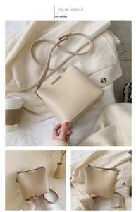 Detail of minimalist off-white bucket bag with elegant gold metal handle and slim strap