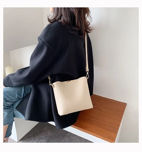 Chic beige bucket bag detail on a model in a minimalist setting with leather texture