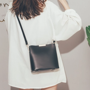 Detail of minimalist black bucket bag with gold hardware worn by a model in casual style