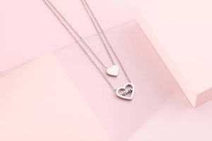 Detail of silver double-layered heart necklace with mom engraving on pink background