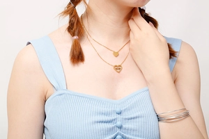 Detail of a layered gold heart necklace and thin silver bracelets on a model
