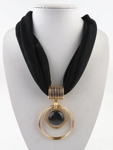 Detail of a large gold concentric ring pendant with black stone on a fabric necklace