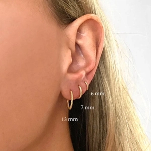 Three sizes of 18k gold plated twisted rope hoop earrings worn on a model's ear