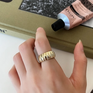 Gros plan d'une bague large dorée avec texture nervurée verticale sur un doigt
