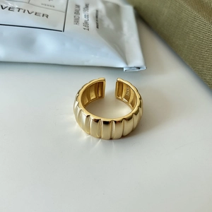 Vue macro d'une bague croissant dorée à nervures sur une surface blanche minimaliste