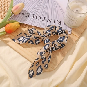 Close-up of leopard print satin scrunchie with bow detail on a rustic wooden tray