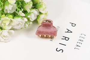 Detail of pink glitter acrylic hair claw with golden metal teeth on aesthetic background