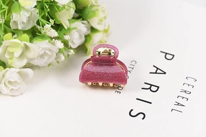 Macro detail of a mini pink glitter hair claw clip with golden metal spring and teeth
