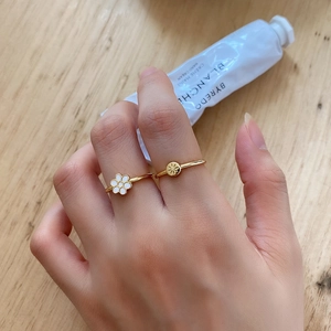 Detail of two gold-plated rings featuring a white daisy motif and sunburst star texture