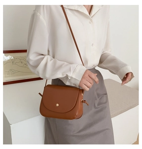 Detail of a brown faux leather crossbody bag with a gold button and knot decoration