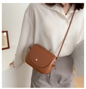 Close-up of vintage brown leather crossbody bag with metallic magnetic buckle on a model