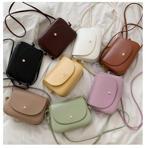 Flat lay of small PU leather crossbody bags in eight various colors on white fabric
