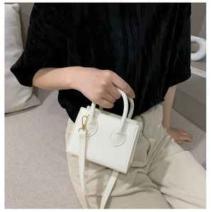 Detailansicht einer weißen Mini-Quadrat-Handtasche mit runden Griffen und Golddetails