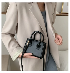 Mini-Umhängetasche aus schwarzem Leder, gehalten von einem Model im beigen Blazer
