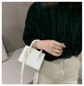 Nahaufnahme einer weißen Mini-Quadrat-Ledertasche mit Rundgriff und goldenen Details
