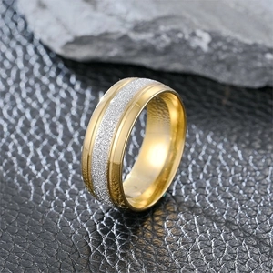 Polished gold titanium steel ring with frosted silver inlay on a dark textured surface