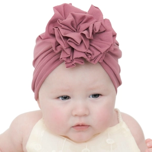 Détail du bonnet turban bébé rose poudré avec grande fleur plissée sur fond blanc immaculé