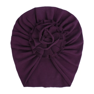 Détail d'un turban bébé en coton tricoté violet foncé avec fleur en tissu plissée