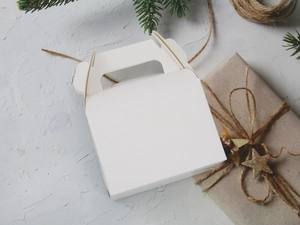 Top-view of white gift box with handle among green pine branches and kraft paper decor
