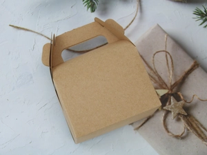 Brown kraft paper candy box with handle on white textured surface with pine needles