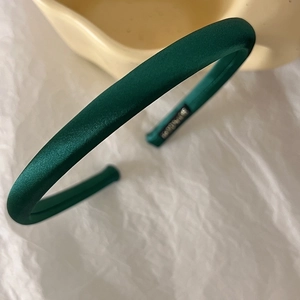 Detail of emerald green fabric sponge headband with a glossy silk texture on cream cloth