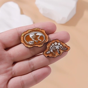 Macro detail of two dinosaur fossil enamel brooches with white bones on amber bases