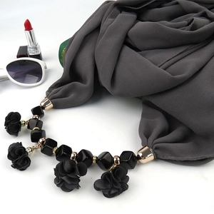 Detail of dark grey scarf with floral pendant and black beads on white background
