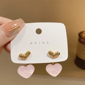 Macro shot of pink pearlescent heart earrings with golden studs on a white card