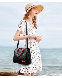 Detail of embossed black leather tote bag with red handles and metal logo tag in outdoor setting