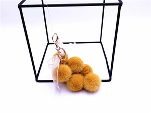 Detail of ginger plush grape keychain with six faux fur balls and a pink silk bow
