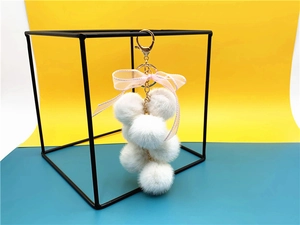 Detail of white plush ball keychain with pink silk bow on metal ring and lobster clasp
