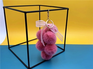Macro detail of a pink plush grape keychain with a soft faux fur ball and ribbon bow
